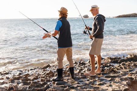 Senior man fishing with his teenage grandson at seasideの写真素材