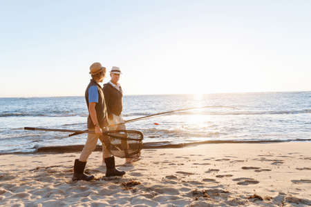 Senior man fishing with his teenage grandson at seasideの写真素材