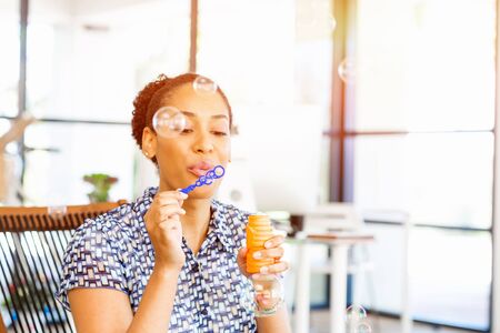 Portrait of beautiful smiling afro-american office worker blowing bubbles in office