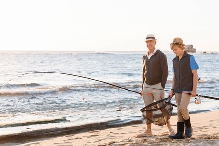 Senior man fishing with his teenage grandson at seasideの写真素材