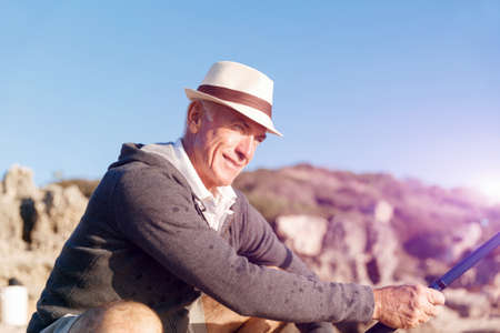 Senior man fishing with rod at seasideの写真素材