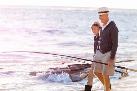 Senior man fishing with his teenage grandson at seasideの写真素材