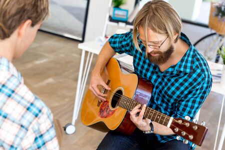 Man in casual clothes playing guitar in office