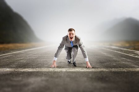 Young businessman in start pose on road ready to run