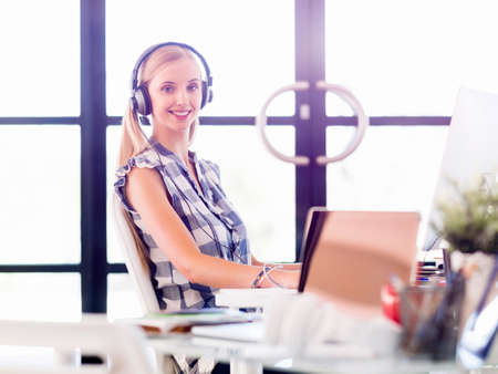 Young woman in casual clothes listening to the music while working on a computerの写真素材