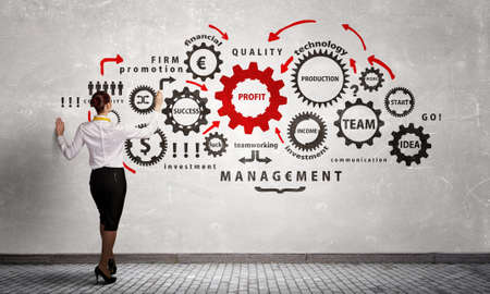 Businesswoman standing with back and drawing gear mechanism on wallの写真素材