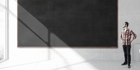 Young man in glasses and checked shirt in room with blackboard. Mixed mediaの写真素材