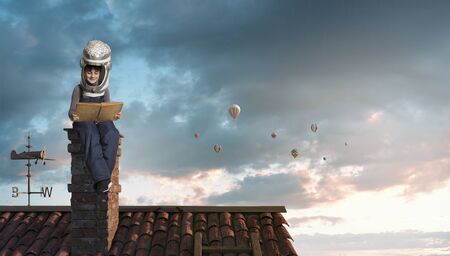 Funny boy in carton helmet reading book and dreaming he is astronautの写真素材