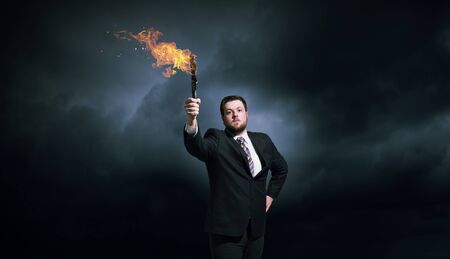 Young businessman in darkness holding burning torch in handの写真素材