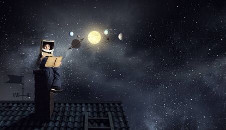 Funny boy in carton helmet reading book and dreaming he is astronautの写真素材