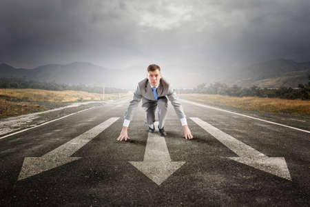 Young businessman in start pose on road ready to runの写真素材