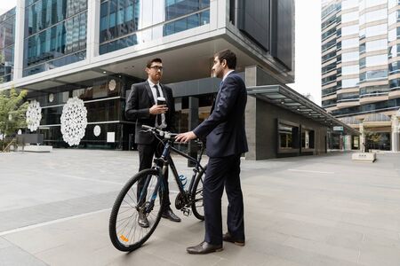 Young businessman with bike talking to his colleague