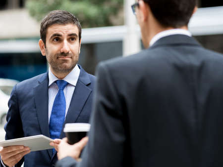 Two businessmen talking outdoors while taking coffee break