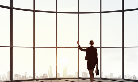 Back view of businesswoman against panoramic office window. Mixed mediaの写真素材