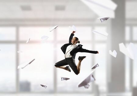 Young cheerful businesswoman in modern office interior dancing like ballerina. Mixed mediaの写真素材