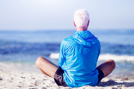 Man in sports wear sitting alone at the beach and having minute of restの写真素材