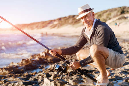Senior man fishing with rod at seasideの写真素材