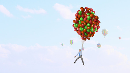 Young businessman flying high in sky on color balloon