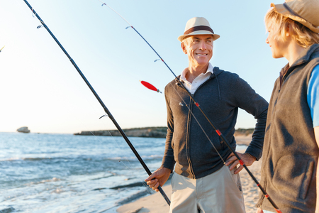 Senior man fishing with his teenage grandson at seasideの写真素材