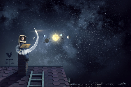 Funny boy in carton helmet reading book and dreaming he is astronautの写真素材