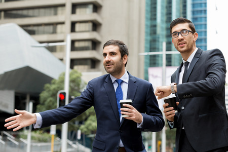 Two young businessmen in suits catching taxiの写真素材