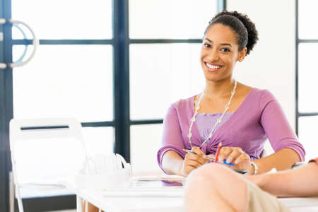 Portrait of beautiful smiling afro-american office worker sitting in officeの写真素材