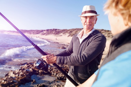 Senior man fishing with his teenage grandson at seasideの写真素材