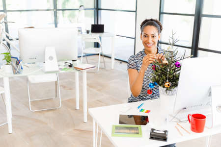 Portrait of beautiful smiling female office worker in office decorating Christmas treeの写真素材