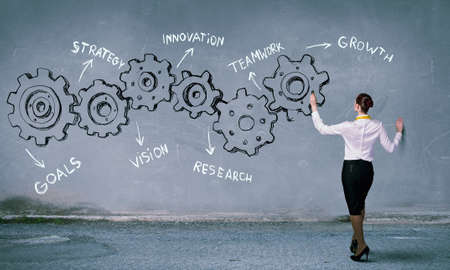 Businesswoman standing with back and drawing gear mechanism on wallの写真素材