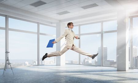 Cheerful businessman in office interior jumping high. Mixed mediaの写真素材