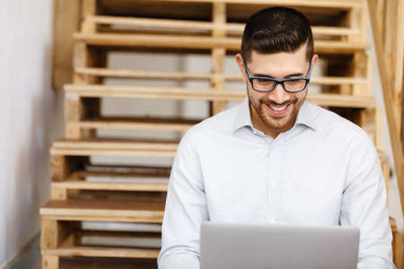 Portrait of young man in casual clothes sitting at the stairs in office