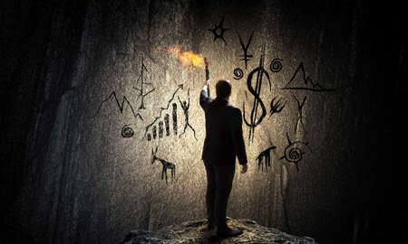 Young businessman in darkness holding burning torch in handの写真素材