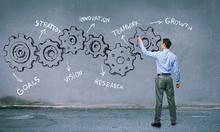 Businessman standing with back and drawing gear mechanism on wallの写真素材