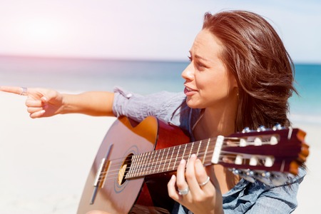 Beautiful young smiling woman playing guitar on beachの写真素材