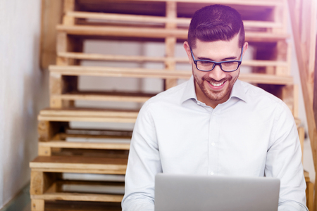 Portrait of young man in casual clothes sitting at the stairs in officeの写真素材