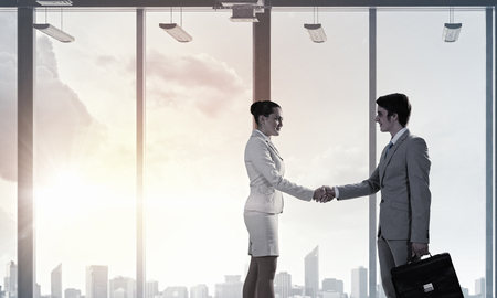 Businessman and businesswoman in modern interior shaking hands. Mixed mediaの写真素材