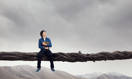 Young man sitting on log above gap. Risk and challenge concept . Mixed media