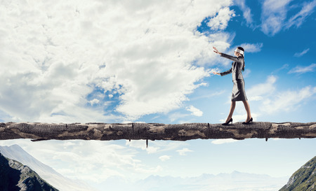 Blind businesswoman walking on wooden log above gap. Risk and challenge concept . Mixed mediaの写真素材