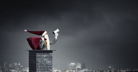 Businessman in Santa hat on house roof shouting in megaphone . Mixed mediaの写真素材