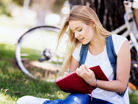 Beautiful young woman writing in her diary in summer parkの写真素材