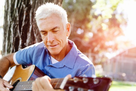 Handsome senior man playing guitar in summer parkの写真素材