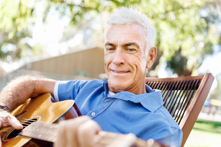 Handsome senior man playing guitar in summer parkの写真素材