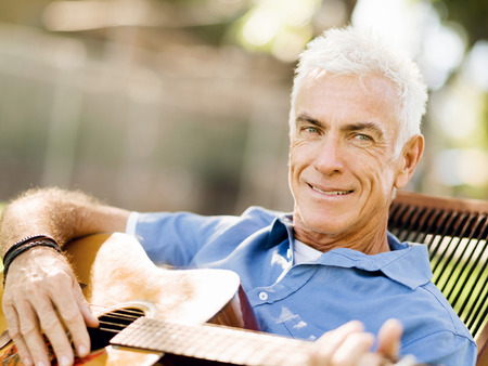 Handsome senior man playing guitar in summer parkの写真素材