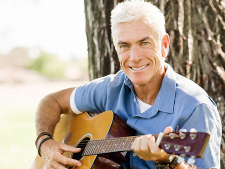 Handsome senior man playing guitar in summer park