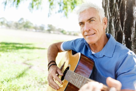 Handsome senior man playing guitar in summer parkの写真素材