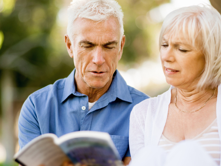 Nice elderly couple outdoors reading book togetherの写真素材