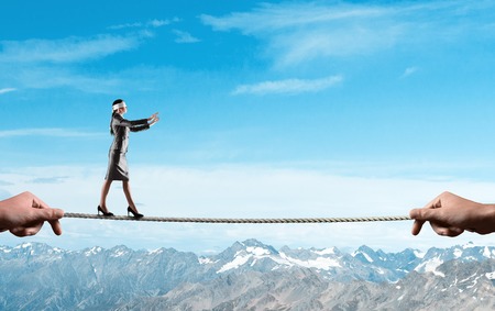 Businesswoman with blindfolder on eyes balancing on the rope