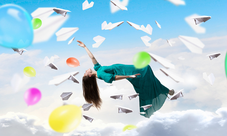 Dreamy beautiful woman in green dress flying in skyの写真素材