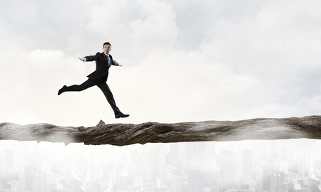 Young successful businessman running on log above gap. Risk and challenge conceptの写真素材