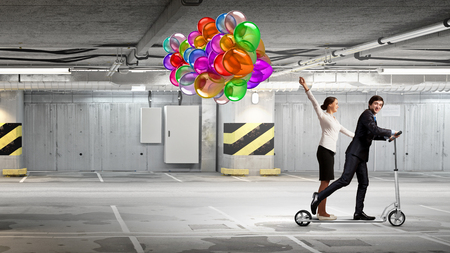 Young cheeful businesspeople riding scooter in office. Mixed mediaの写真素材